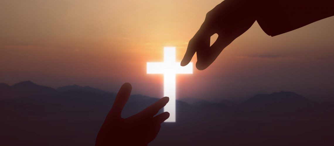 Jesus Christ giving a helping hand to human with a sunset sky background